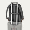 Gray backpack with a rear strap over suitcase handle on a white background