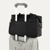 Black tote secured over suitcase handle using rear strap, on a white background