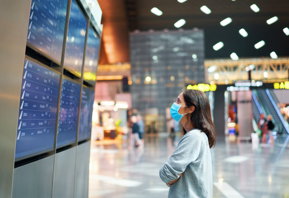 woman wearing mask looking at flight screen
