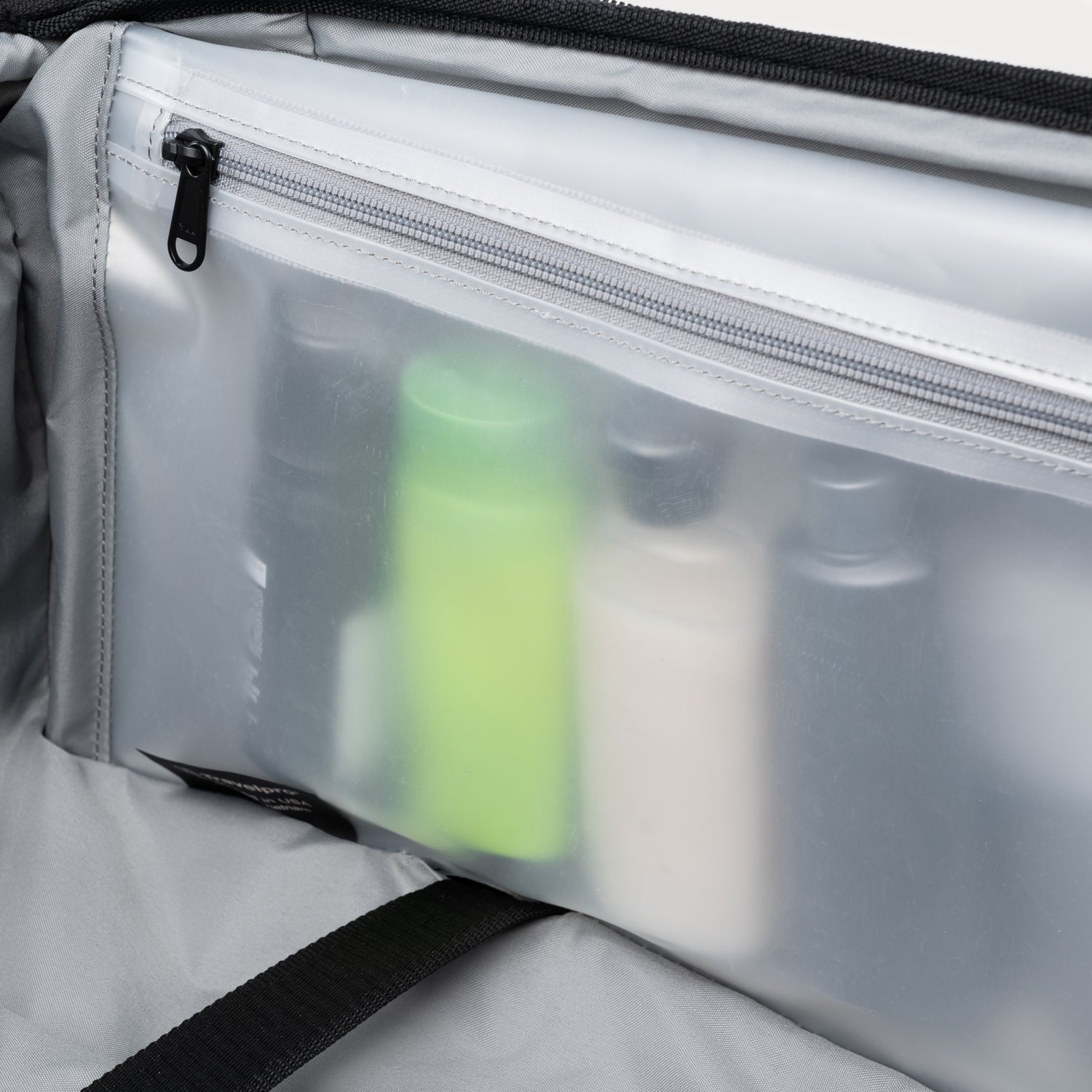 Vue claire de l'intérieur de la valise, avec une pochette translucide à fermeture éclair contenant des flaconsTaille placés à la verticale.