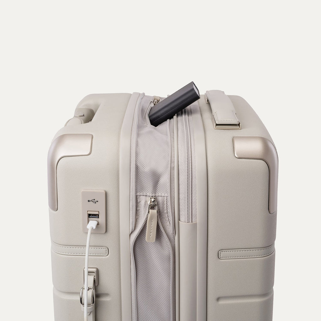 Charging cable plugged into the external USB port on the Travelpro Platinum Reserve Compact Carry-On Hardside Spinner in Sandstone