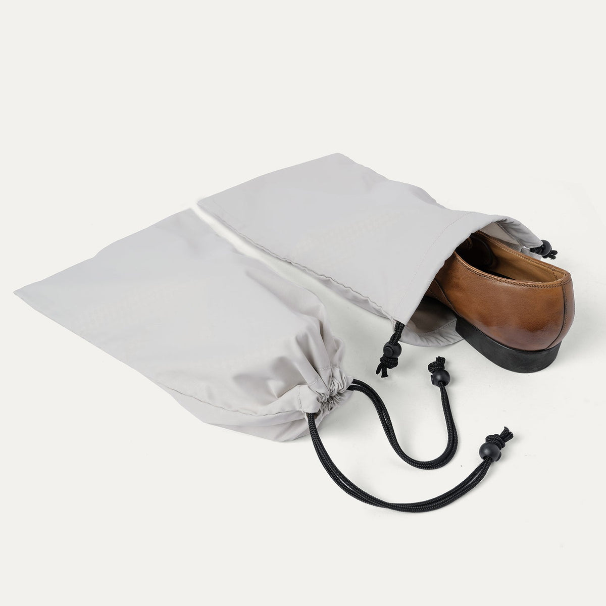 Drawstring shoe bag included with the Travelpro Platinum Reserve Medium Check-In Hardside Spinner in Black Dust, shown holding a pair of shoes