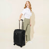 A person pulling a black carry-on spinner luggage with telescopic handle.