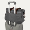 Grey tote secured over suitcase handle using rear strap, on a white background