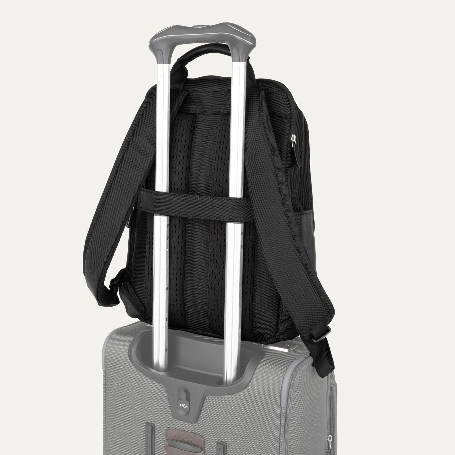 Black backpack with a rear strap over suitcase handle on a white background