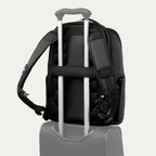 Black backpack with a black strap over suitcase handle on a white background